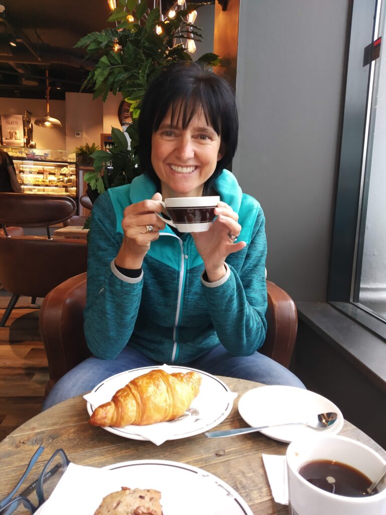 Strickarin sitzt in einer Bar und trinkt Kaffee und genießt ein Croissant